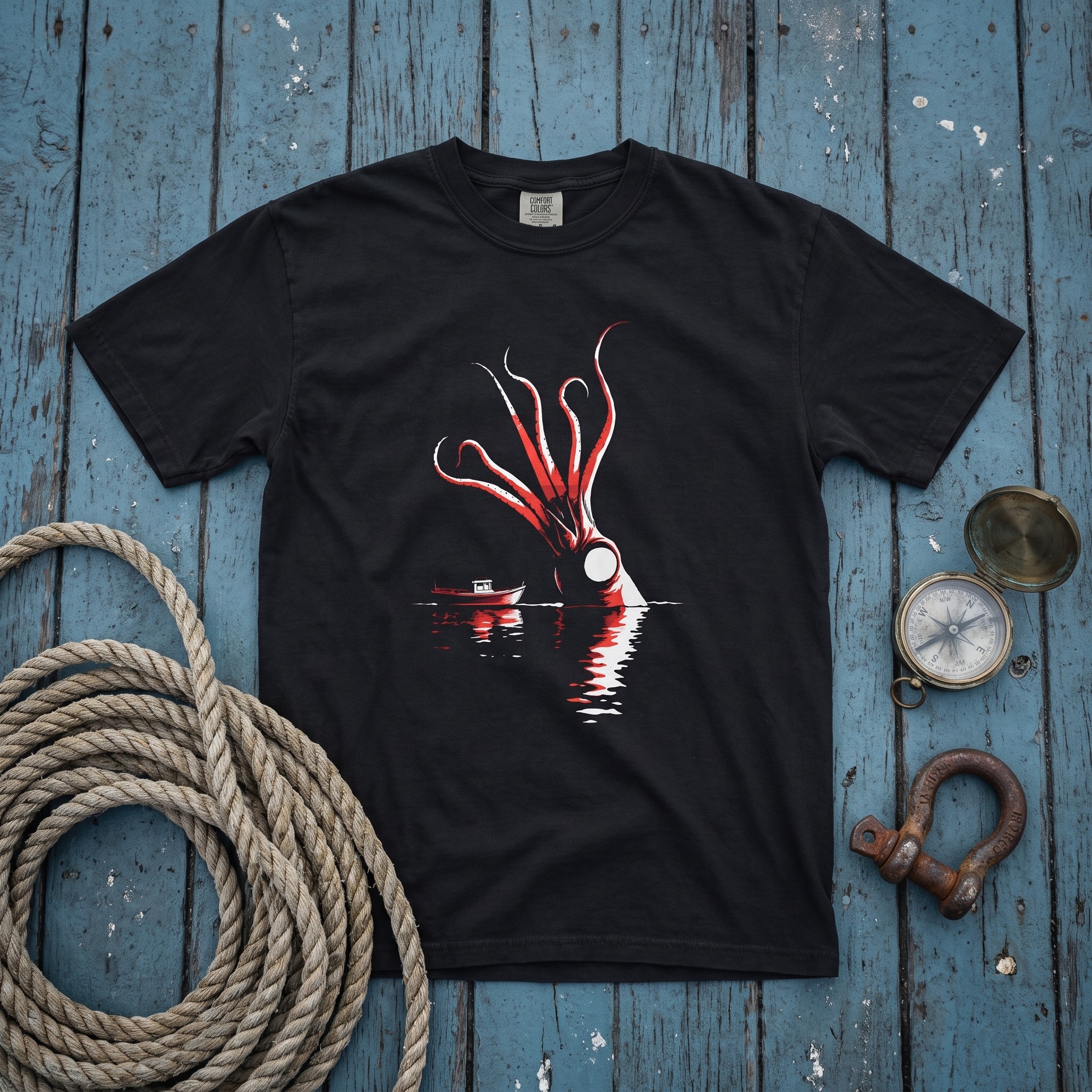 The Kraken tee laid flat on the blue deck of a North Atlantic fishing boat beside coiled rope, a brass compass and a rusted shackle