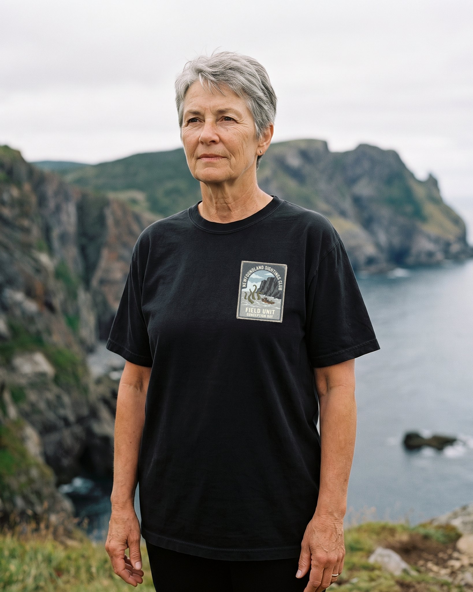 A person wearing the Newfoundland Sightings Club tee in black on location near Conception Bay, Newfoundland