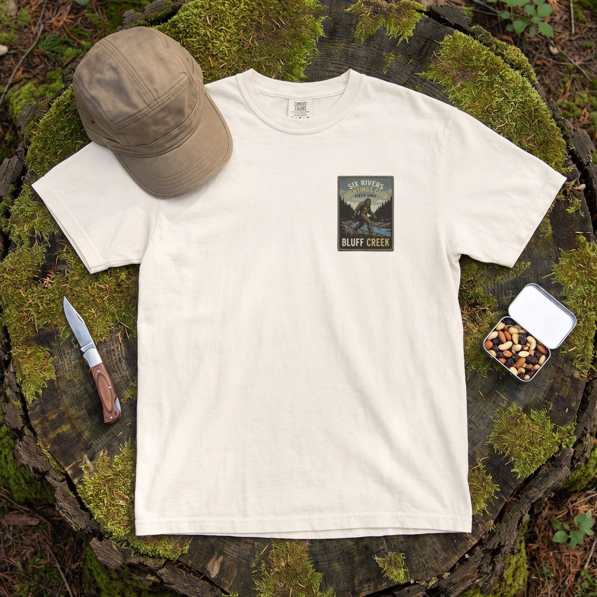 The Six Rivers Sightings Club tee in ivory laid flat with field kit from the Bigfoot file